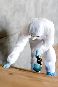 A pest control technician in protective gear inspects a wooden floor in a construction apartment. 